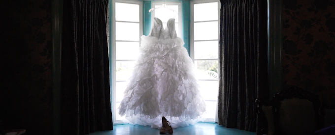 Wedding dress hangs in sunny window during wedding video.